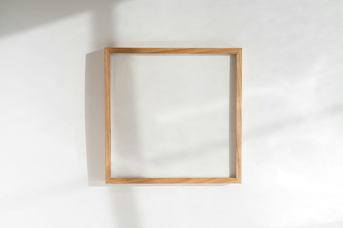 An empty light wooden frame hanging on a white wall